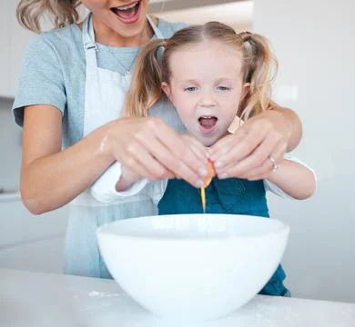 Mother helping daughter crack egg into bowl while baking together in the kitchen Stock Photos
