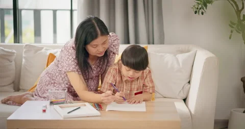 Mother helping son with Down syndrome drawing together on sofa at home. Stock Footage 310175256