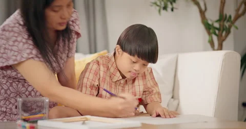 Mother helping son with Down syndrome drawing together on sofa at home. Stock Footage 310175288