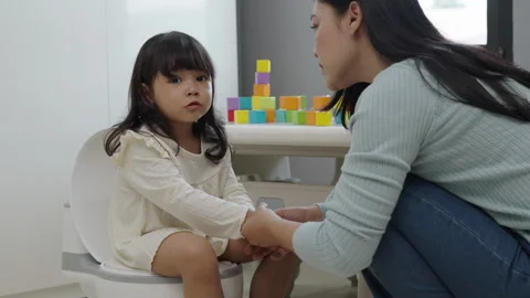 Mother is helping toddler gir learning sit on toilet wc seat at home Stock Footage 314081307