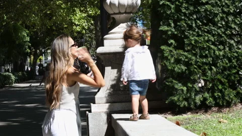 Mother Helps Child Practice Walking on Outdoor Stone Platform in Summer Park Stock Footage 346416070