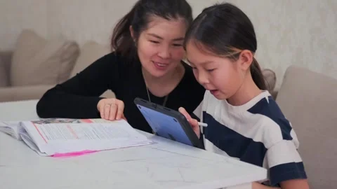 Mother helps daughter learn using tablet and school materials, modern digital Stockbeeldmateriaal 333483627
