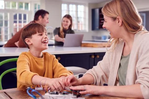 Mother Helps Son With Electronics Project Sitting At Kitchen Table At Home With Stock Photos