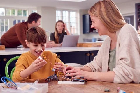 Mother Helps Son With Electronics Project Sitting At Kitchen Table At Home With Stock Photos