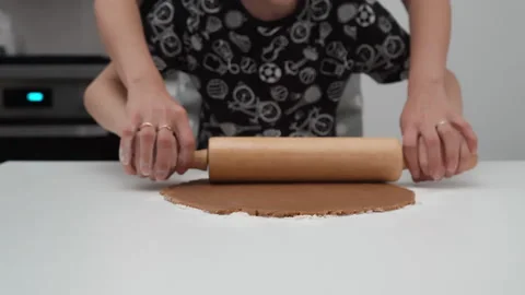 Mother helps son roll out gingerbread cookie dough with rolling pin on table Video stock 337500881