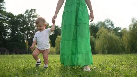 Mother helps toddler learn to step. Family moment in nature as toddler learns to Stock Footage 317016535