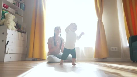 Mother helps toddler take first steps. Toddler learns to walk with mother Stock Footage 345337911