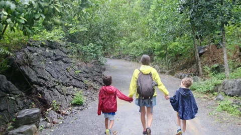 Mother, her backpack-clad children, and their colorful raincoats Stock Footage 252036115