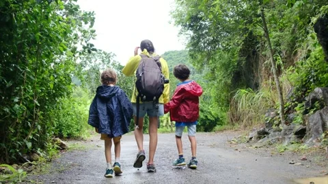Mother, her backpack-clad children, and their colorful raincoats Stock Footage 252036192