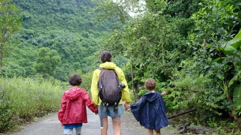 Mother, her backpack-clad children, and their colorful raincoats Stock Footage 252036220