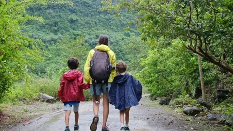 Mother, her backpack-clad children, and their colorful raincoats Stock Footage 252036231