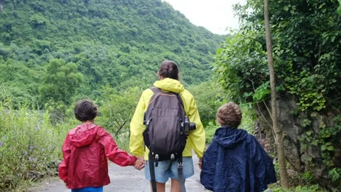Mother, her backpack-clad children, and their colorful raincoats Stock Footage 252036238