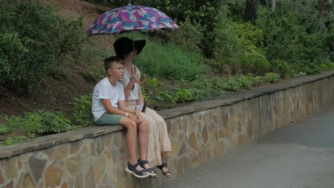 Mother with her son sitting under umbrella in park Video stock 160109017