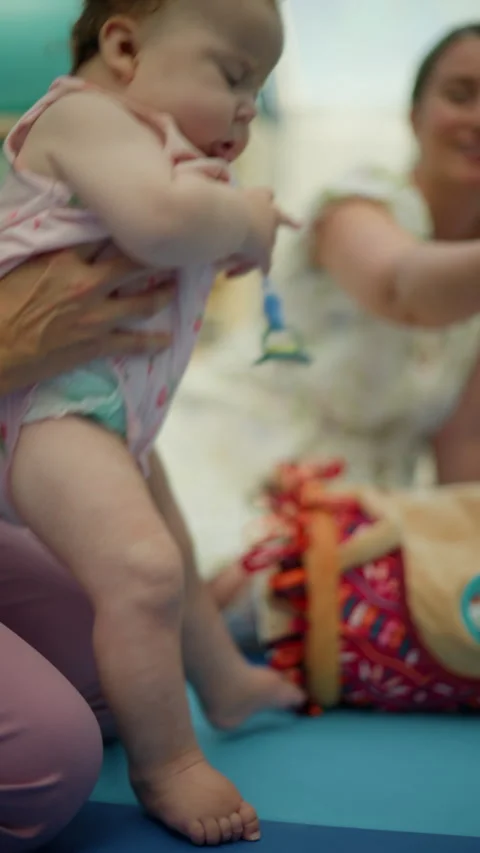 Mother holding baby supporting first steps. Baby wearing pacifier and pink Видео 343138658