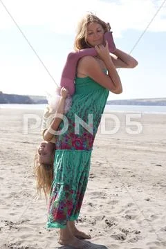 Mother Holding Daughter Upside Down On Beach, Wales, Uk