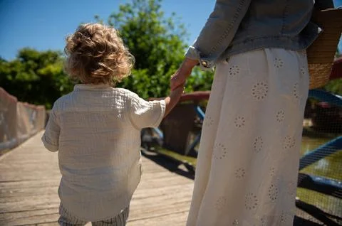 Mother holding son's hand while walking across a sunny wooden bridge in a par Stockfoto's