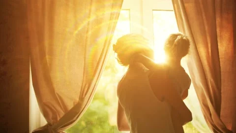 Mother holds and hugs her small daughter near the window at home, happy family Stock Footage