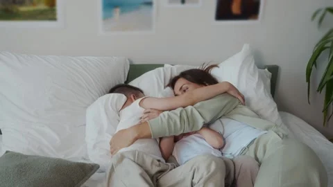 Mother hugging two sons while lying on bed family warmth and care Video stock 316578458