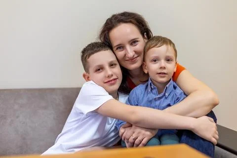 Mother hugging two sons while sitting on a couch. Stock Photos