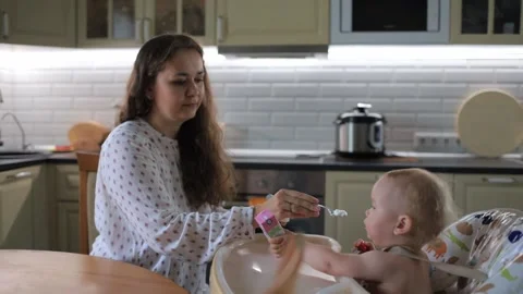 Mother in kitchen feeds with spoonful of small child Stock Footage 131641732