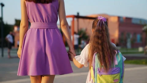 Mother leads child with school backpack playground park. schoolgirl girl holding Stock Footage 248933720