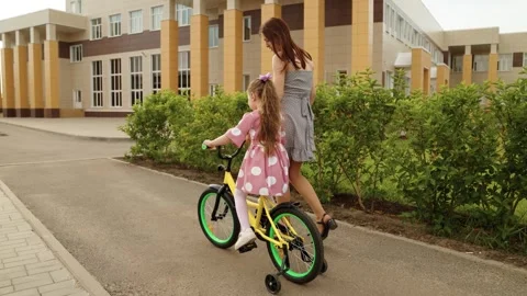 Mother learning help cute little daughter riding on bike on road at schoolyard Stock Footage 275916744