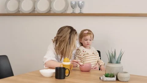 A mother lovingly feeds her child in a cozy kitchen, highlighting their strong Stock Footage 312218993