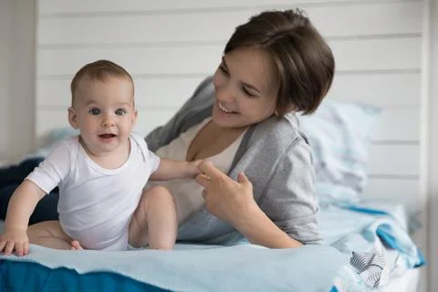 Mother lying on bed, holding tiny arm of beautiful newborn Stock Photos