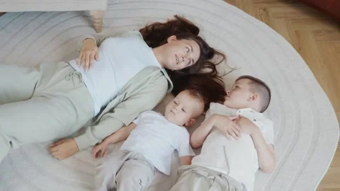Mother lying on carpet with two sons smiling and enjoying family time Stock Footage 315748046
