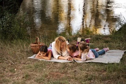 Mother Lying with her Three Daughters by the River Having a Picnic Stock Photos
