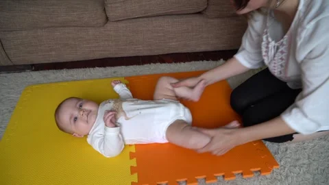 Mother makes exercises with 4- 6 month baby laying on a carpet, looking at the Stock Footage 264086551