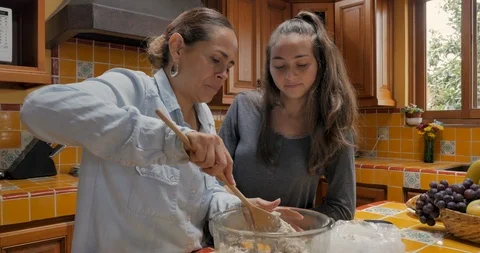 Mother mixing dough while her teenager daughter watches and learns Видео 94172802