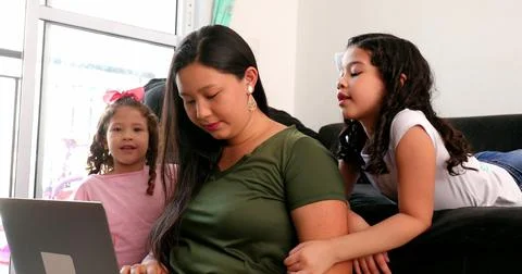 Mother multi-tasking, using computer laptop at home while parenting two child Stock Photos