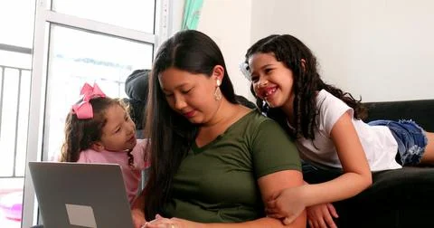 Mother multi-tasking, using computer laptop at home while parenting two child Foto stock