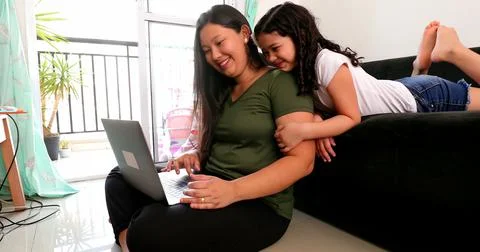 Mother multi-tasking, using computer laptop at home while parenting two child Foto stock