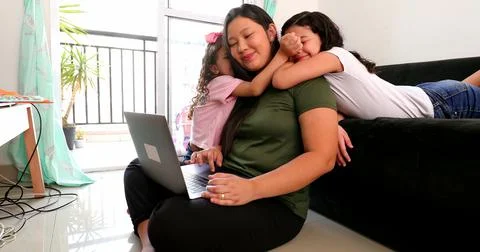 Mother multi-tasking, using computer laptop at home while parenting two child Foto stock