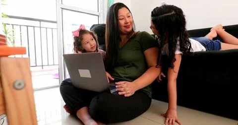 Mother multi-tasking, using computer laptop at home while parenting two child Foto stock