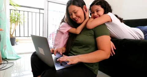 Mother multi-tasking, using computer laptop at home while parenting two child Foto stock