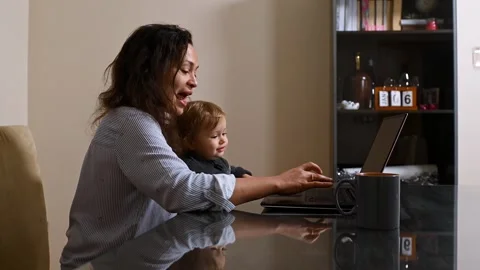 Mother multitasking with child while working from home on laptop Stock Footage 297355092
