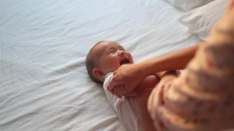 Mother play with baby's arms while he's lying on the bed Stock Footage 201113095