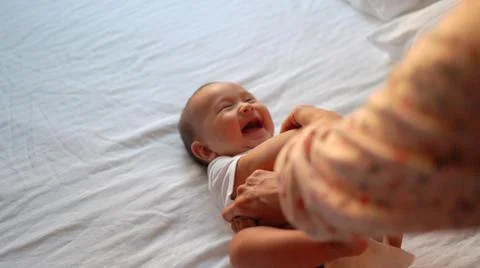 Mother play with baby's arms while he's lying on the bed Stock Photos