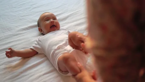 Mother play with baby's legs while he's lying on the bed Stock Footage 201113629