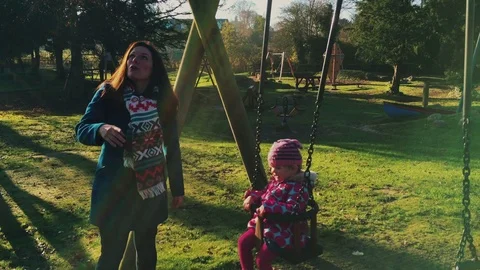 Mother playing and pushing cute toddler daughter on playground swing Stock Footage 76570071