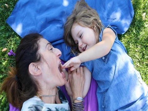 Mother playing bite her daughter hand lying on the grass Stock Footage 80587344