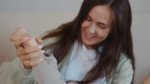 Mother playing with toddler on knees holding his bare feet with love Stock Footage 316578404