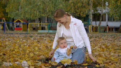 Mother plays with a child  throws maple yellow leaves sitting on the ground. Video stock 130505797
