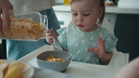 Mother Pours Corn Flakes for Breakfast into her Little Baby Daughter's Bowl Stock Footage 250338437
