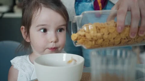 Mother Pours Corn Flakes for Breakfast into her Little Baby Daughter's Bowl Stock Footage 251131561