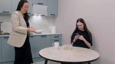 Mother preparing breakfast while daughter is using smartphone Stock Footage 306904826