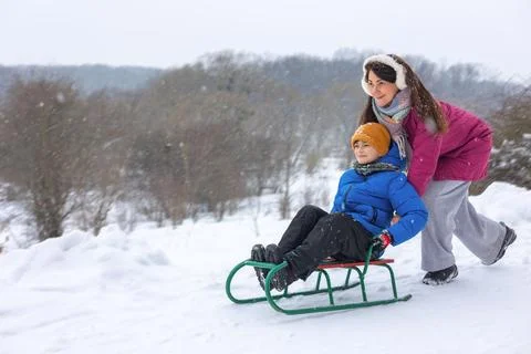 Mother pulling her young son on a sled in a snowy winter park. Family Stock Photos